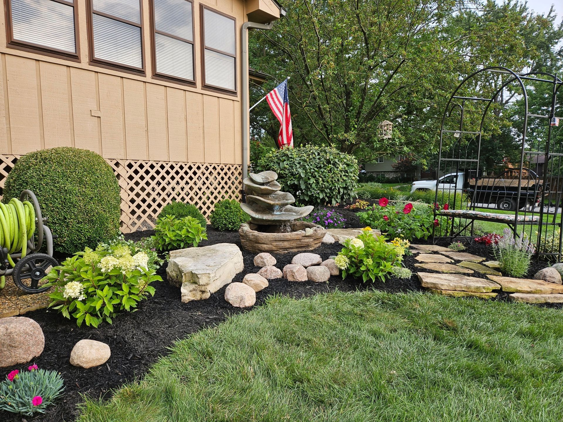 A garden with a fountain and a flag in front of a house.