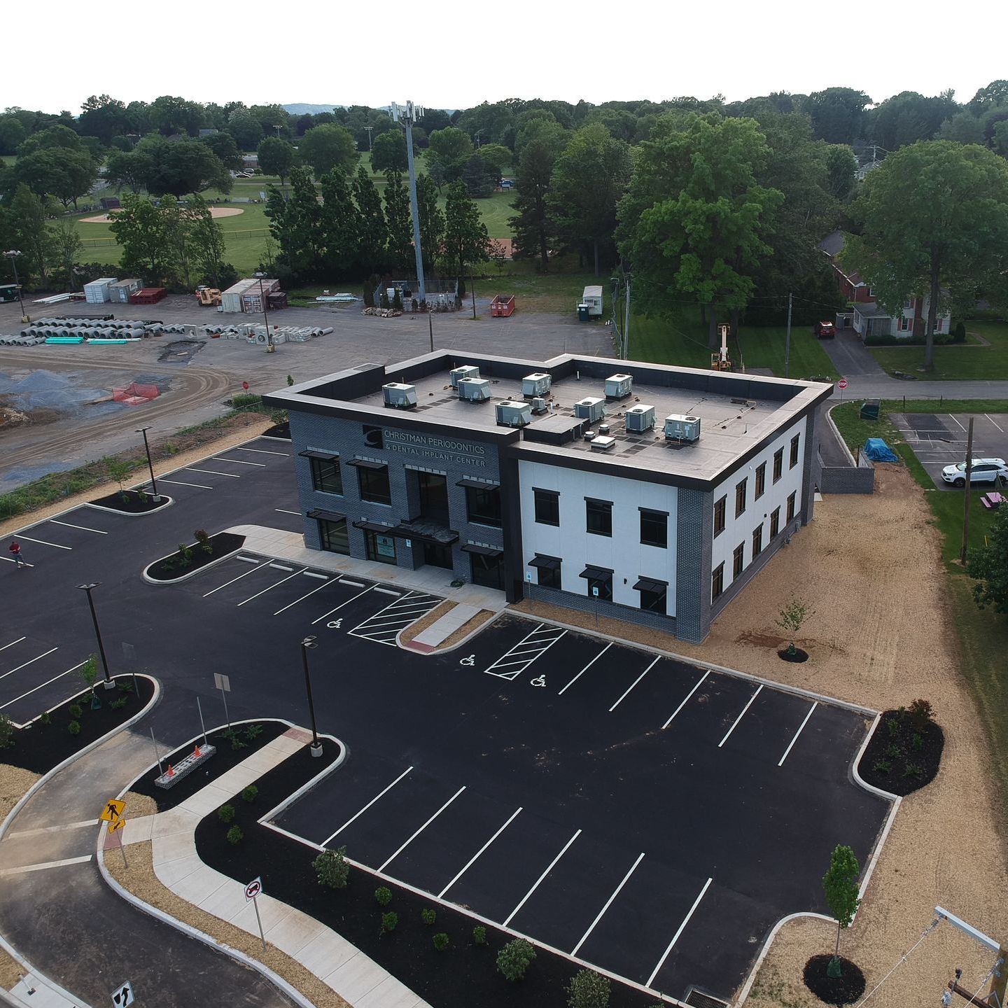 Aerial view of a two-story modern building with a parking lot and surrounding greenery.