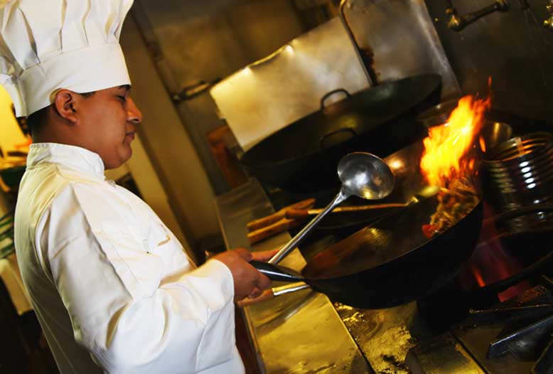 A chef is cooking food in a wok in a kitchen.