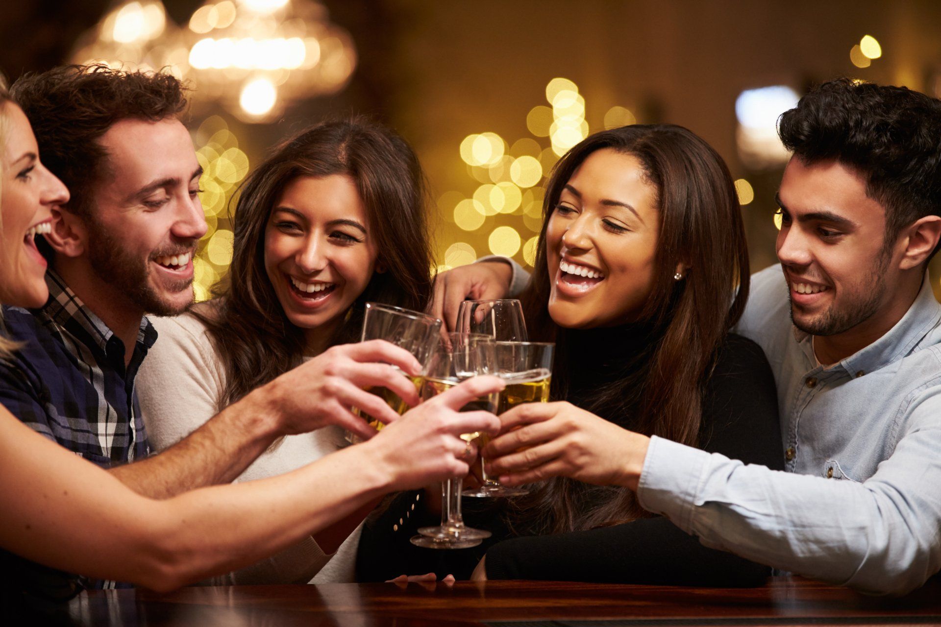 A group of people are toasting with wine glasses at a bar.