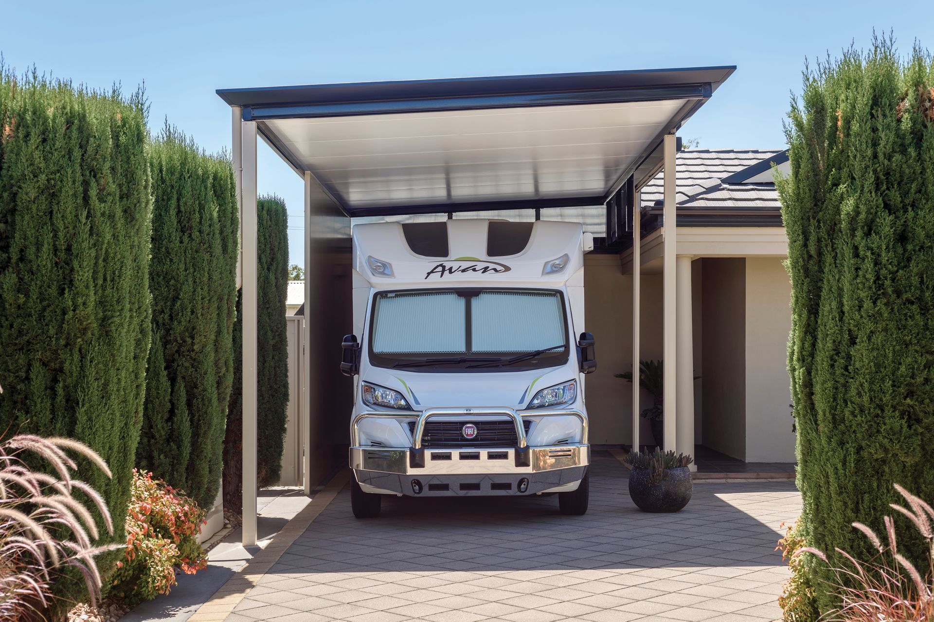 RV parked under a carport in a paved driveway, flanked by green hedges — Precision Patios Toowoomba In Toowoomba, QLD