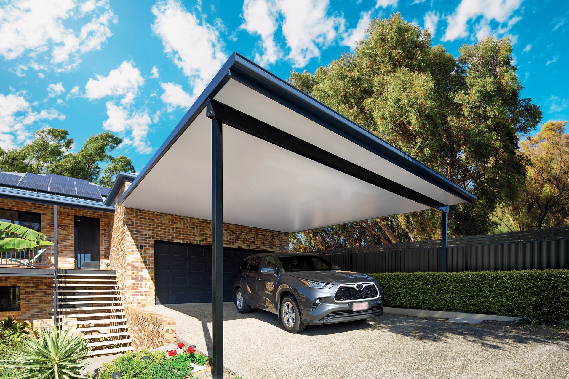 Car parked under a carport attached to a brick house. Blue sky, trees, and gravel driveway — Precision Patios Toowoomba In Toowoomba, QLD