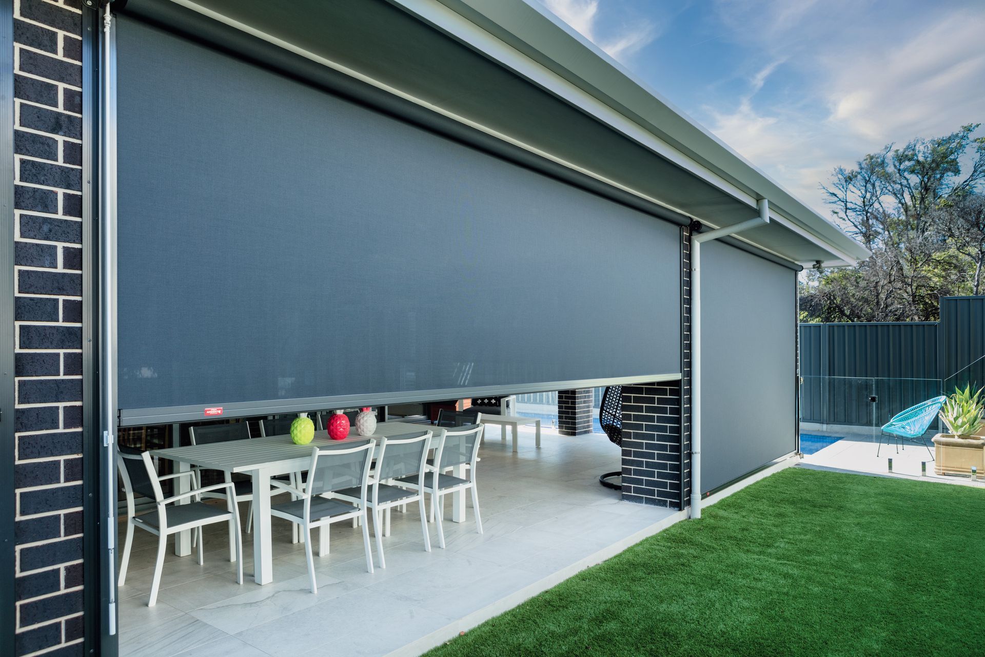 Large retractable sunshade partially open, covering an outdoor dining area. Grey fabric, brick and green lawn visible  — Precision Patios Toowoomba In Toowoomba, QLD
