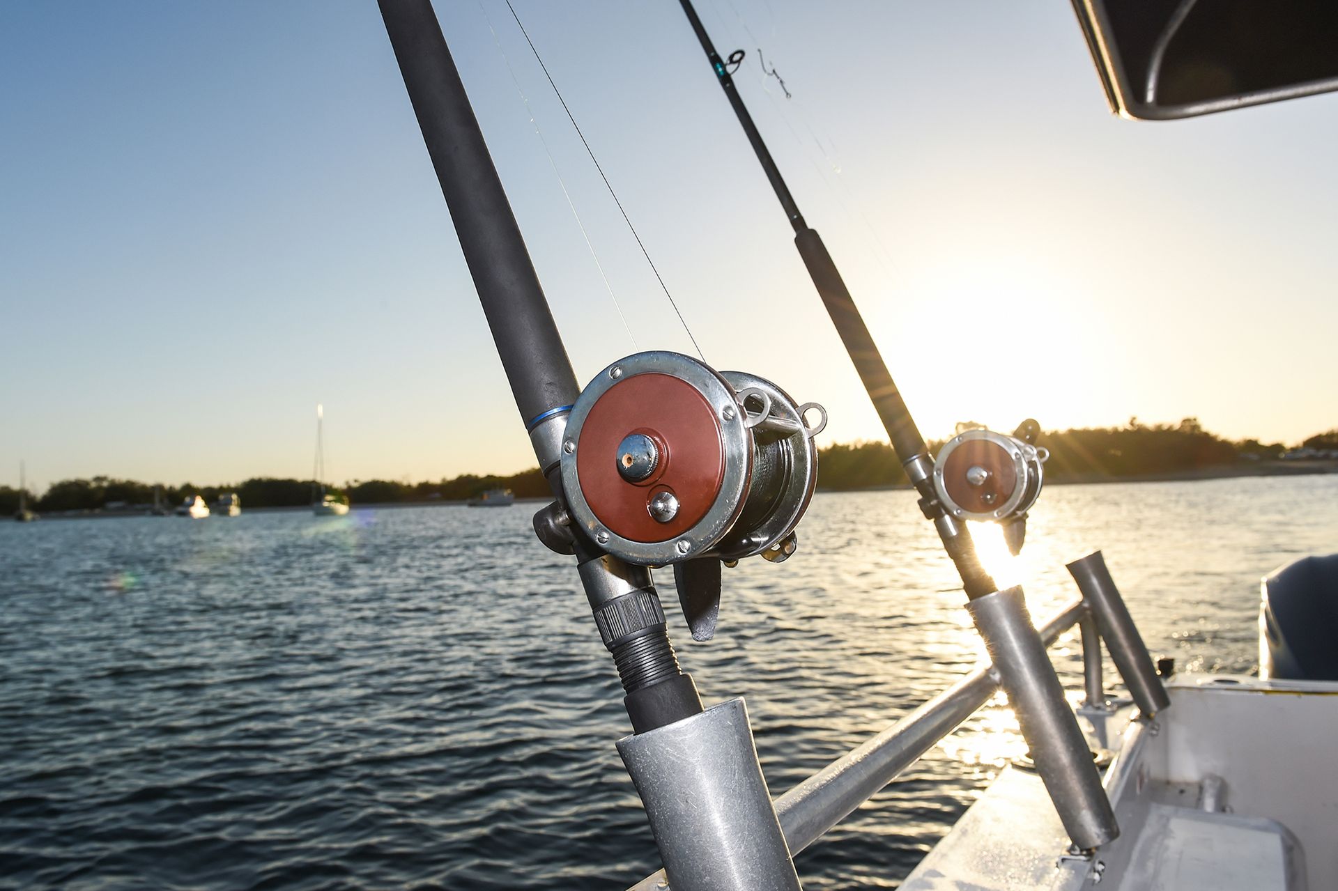 Fishing rods mounted on a boat, with a sunset over the water.