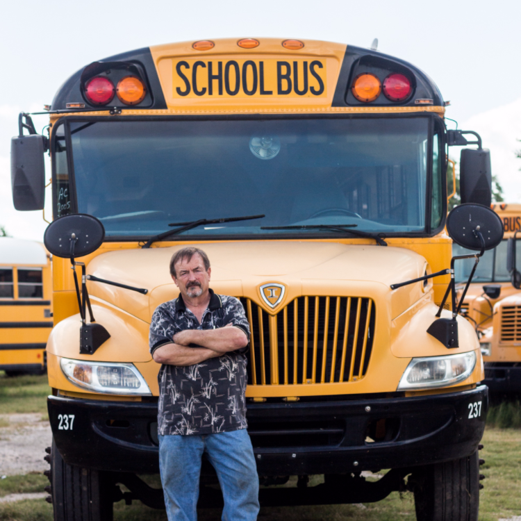 A man stands in front of a yellow school bus