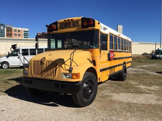 A yellow school bus is parked in a gravel lot.