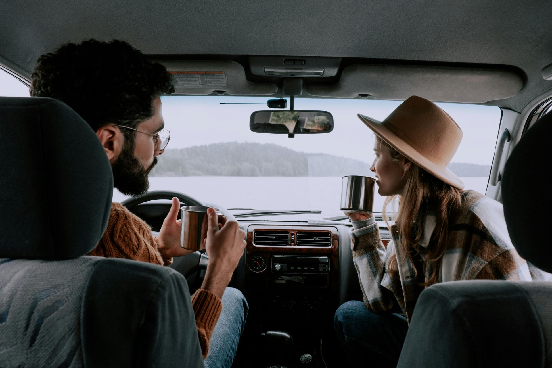 A man and a woman are sitting in the back seat of a car drinking coffee.