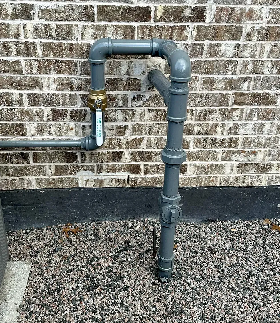 A gray pipe is attached to a brick wall.
