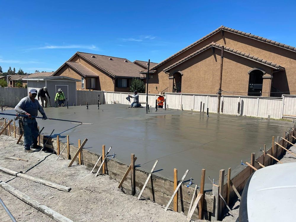 A group of construction workers are working on a concrete floor in front of a house.