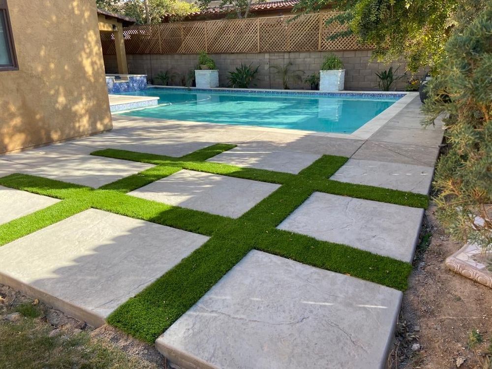 A swimming pool with a concrete walkway surrounded by artificial grass.
