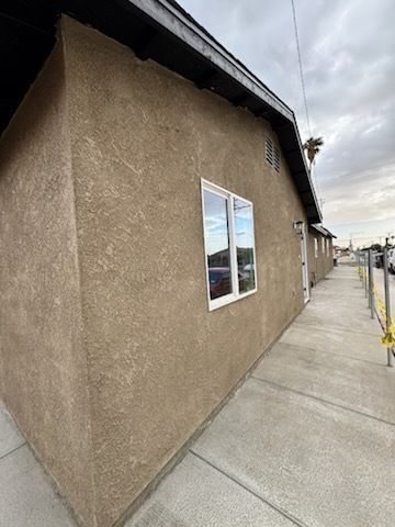 The side of a house with two windows and a sidewalk.