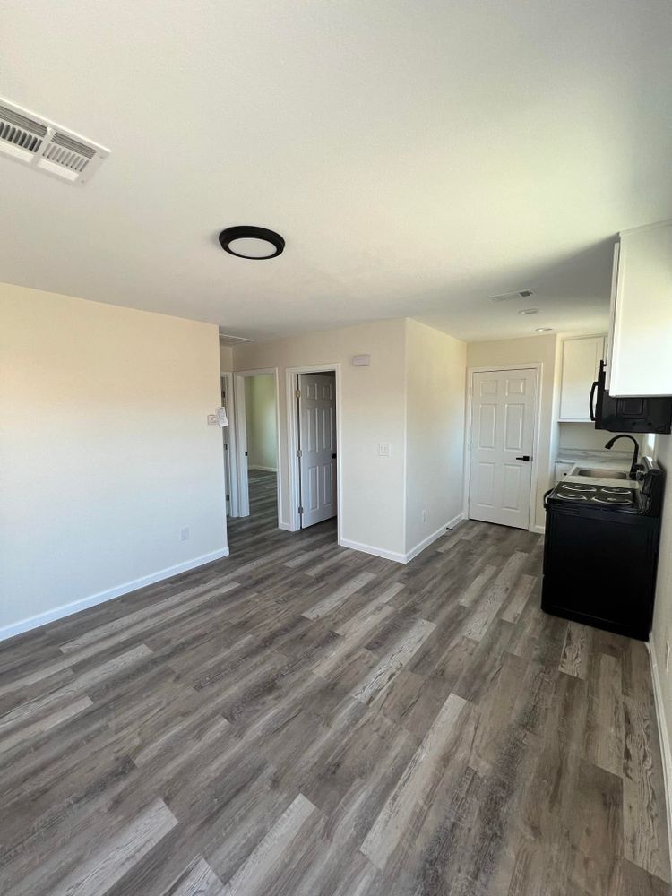 An empty living room with hardwood floors and a kitchen.