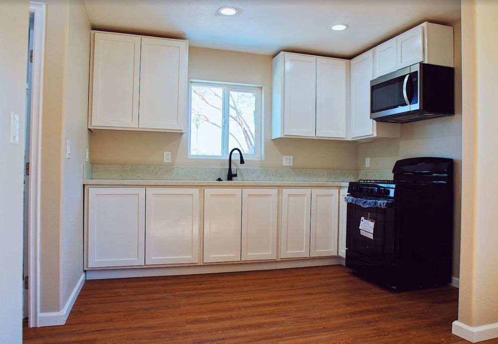 A kitchen with white cabinets , a black stove and a microwave.