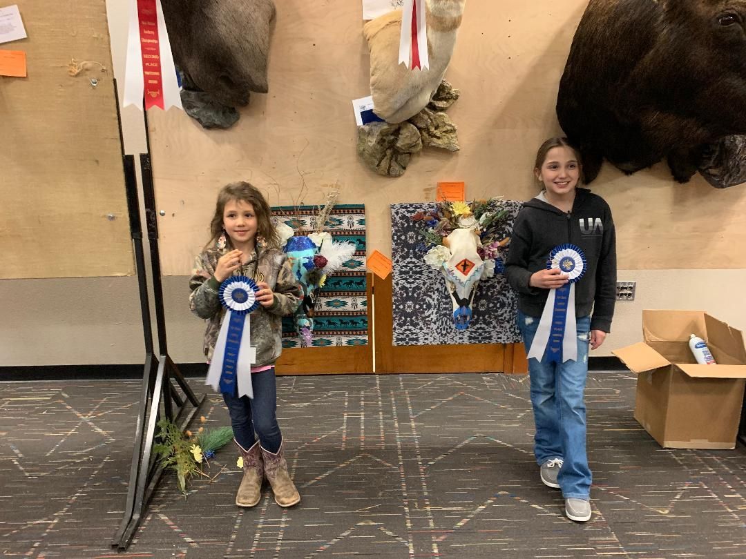 Two young girls are standing next to each other in a room holding ribbons.
