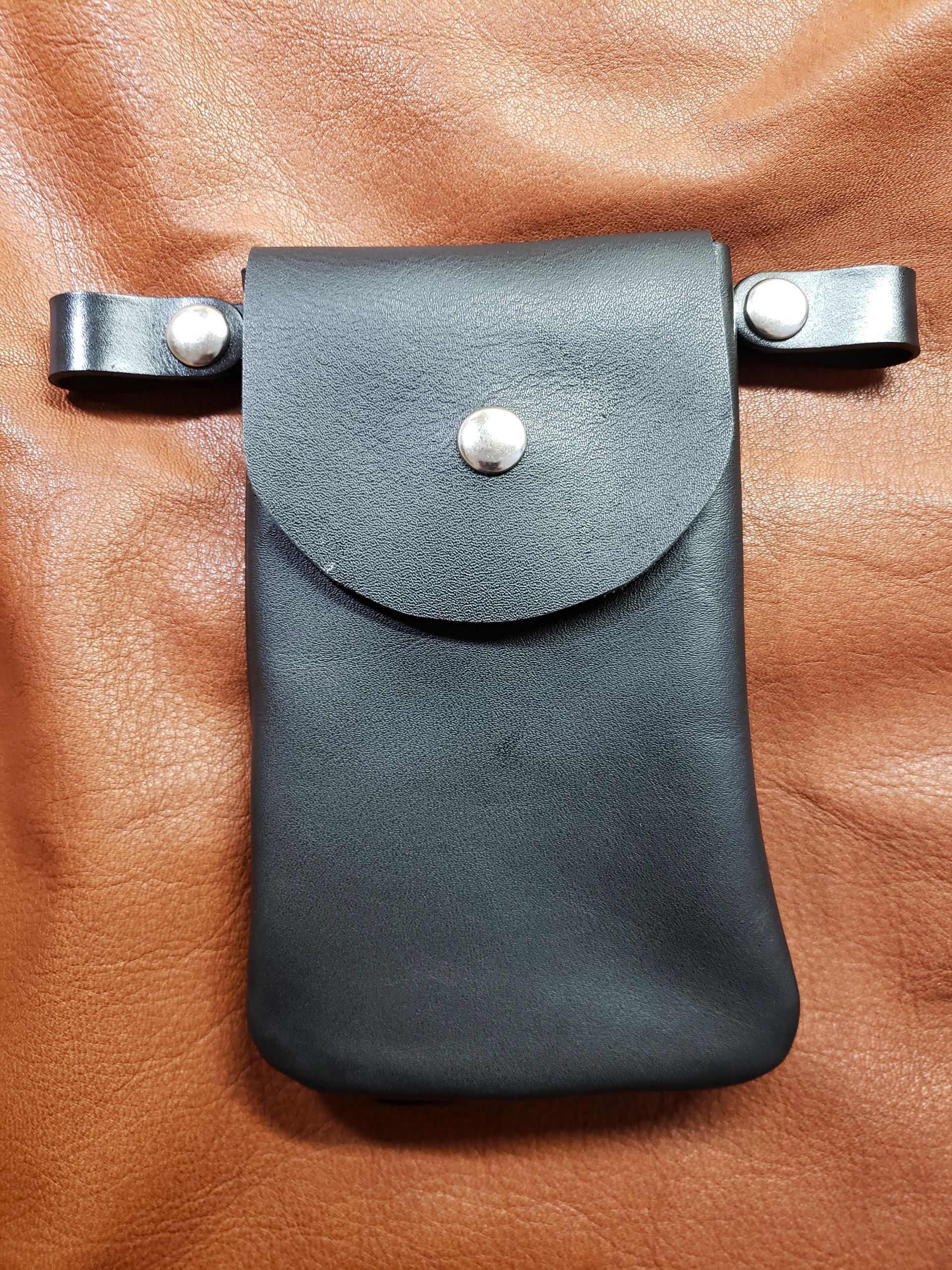 A black leather belt pouch with a snap-button closure and two horizontal belt loops, set against a brown leather background.