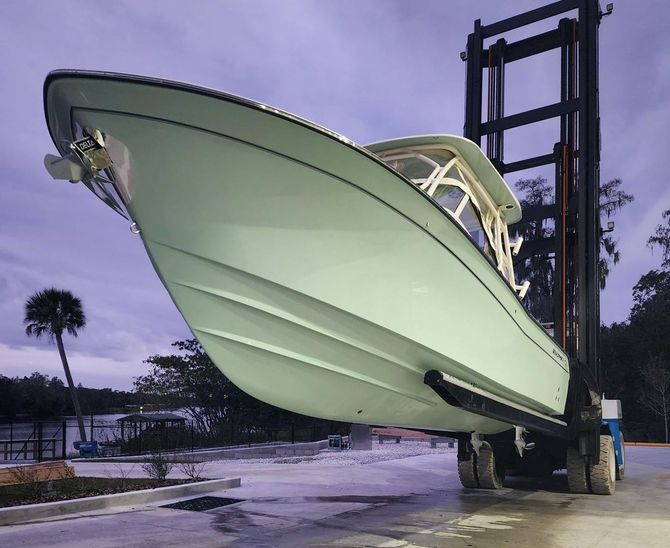 A boat is being lifted by a forklift in a parking lot at Riverview Marina