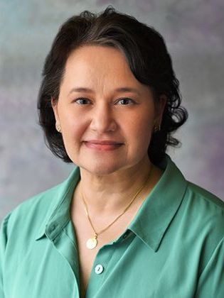 A woman wearing a green shirt and a gold necklace is smiling for the camera.
