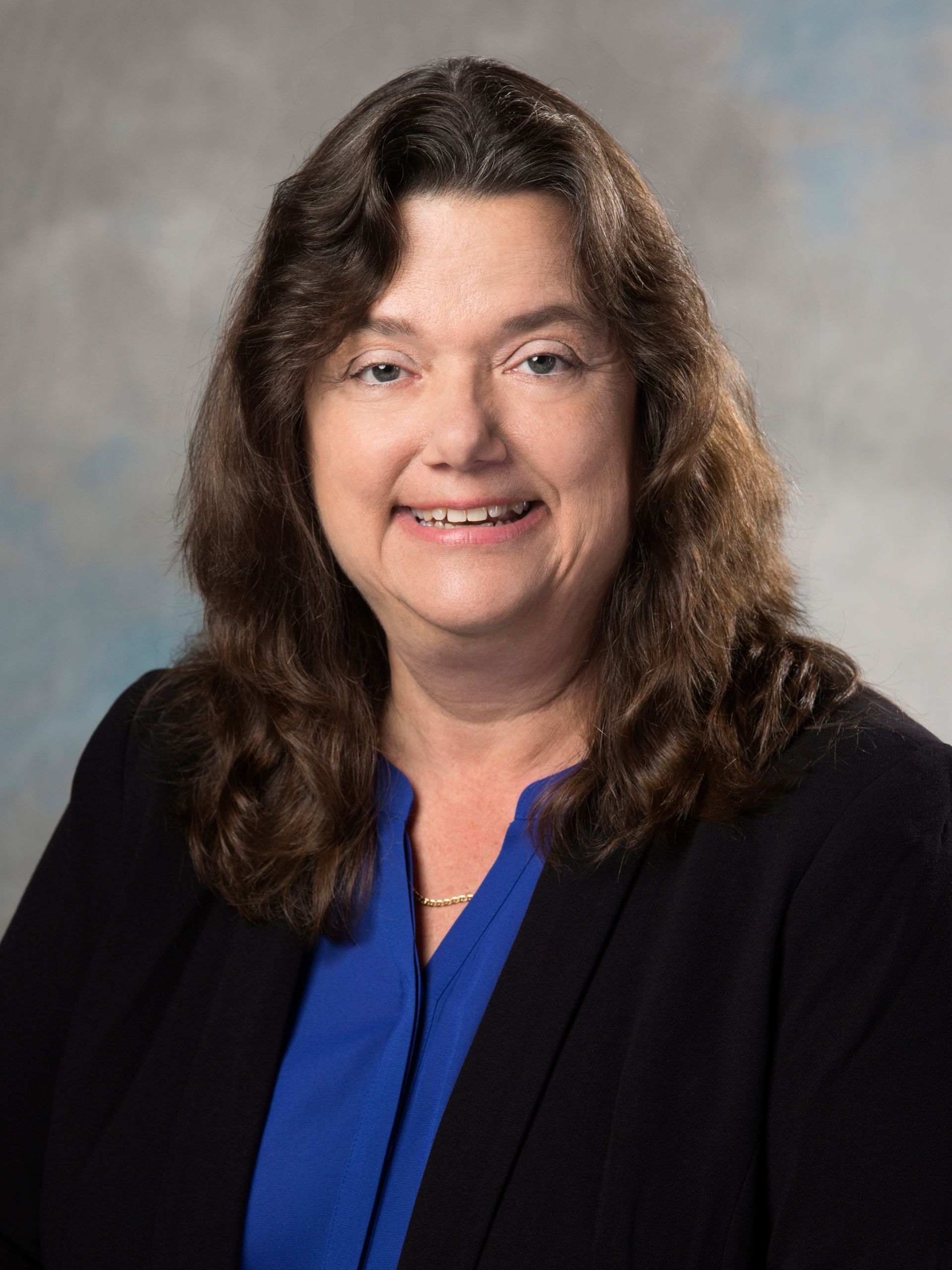 A woman in a blue shirt and black jacket is smiling for the camera.