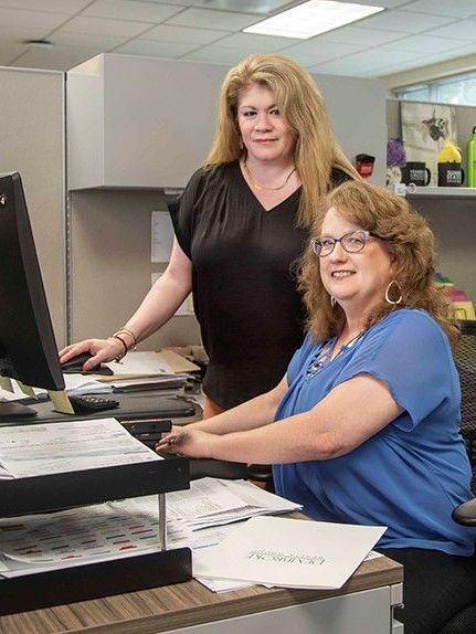 Two women are sitting at a desk in front of a computer.