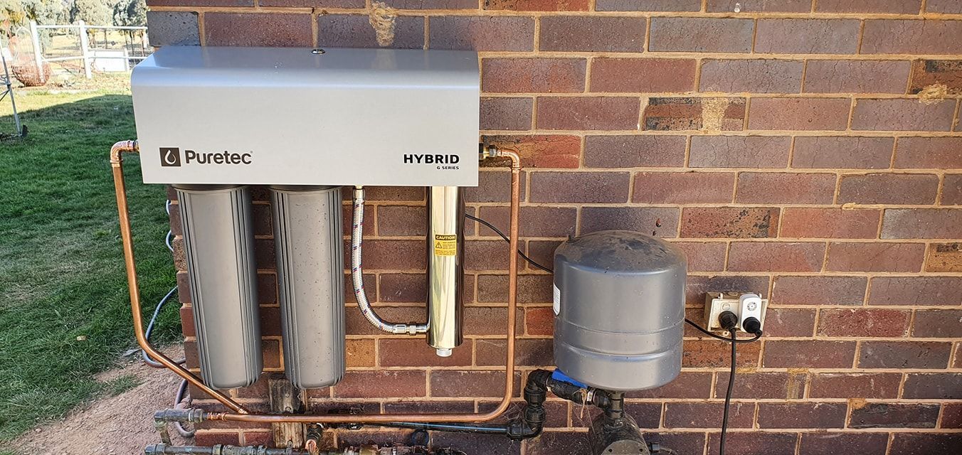 Water filtration system mounted on a brick wall, with pipes, filters, and a storage tank. — Mi Plumber Wagga Wagga in Lake Albert, NSW