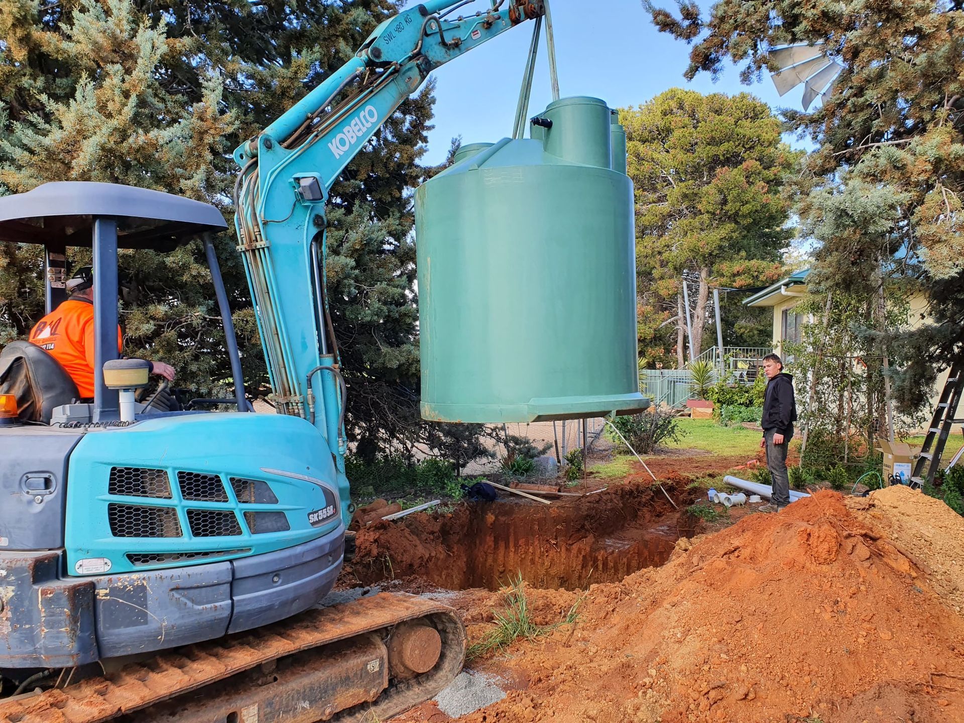 Mini Excavator Lowering a Green Water Tank — Mi Plumber Wagga Wagga in Lake Albert, NSW