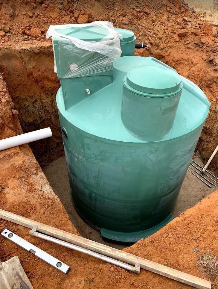 Green septic tank installed in a dirt pit, with white pipe and construction tools visible. — Mi Plumber Wagga Wagga in Young, NSW