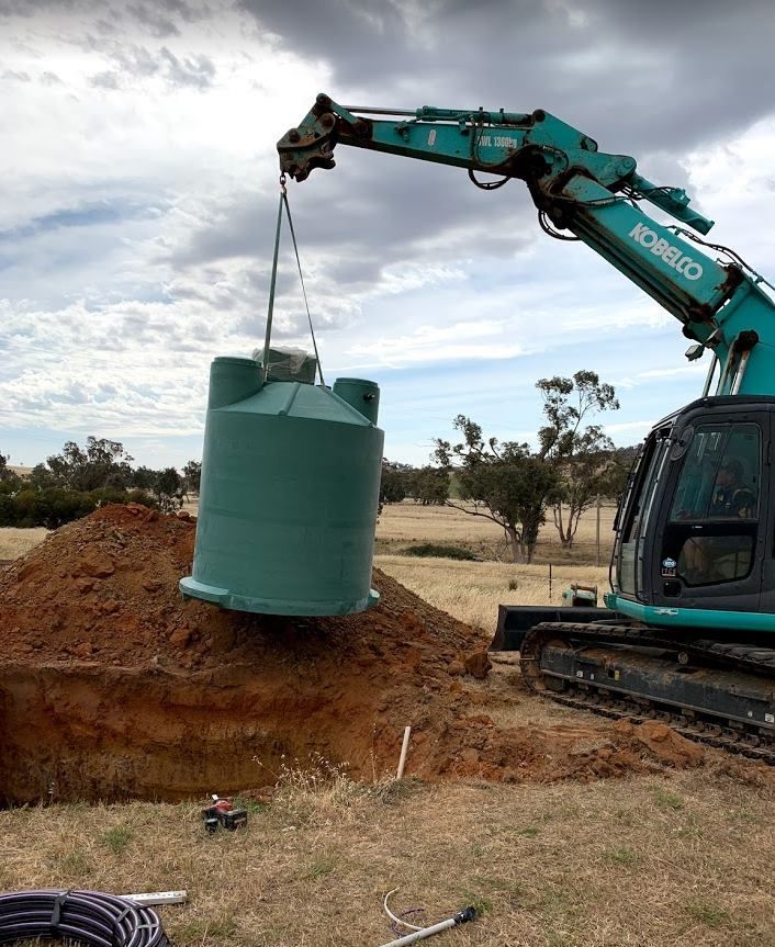An Excavator Lifts a Green Water Tank — Mi Plumber Wagga Wagga in Lake Albert, NSW