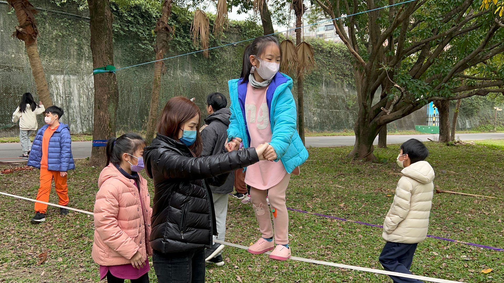A group of children are playing on a tightrope in a park.