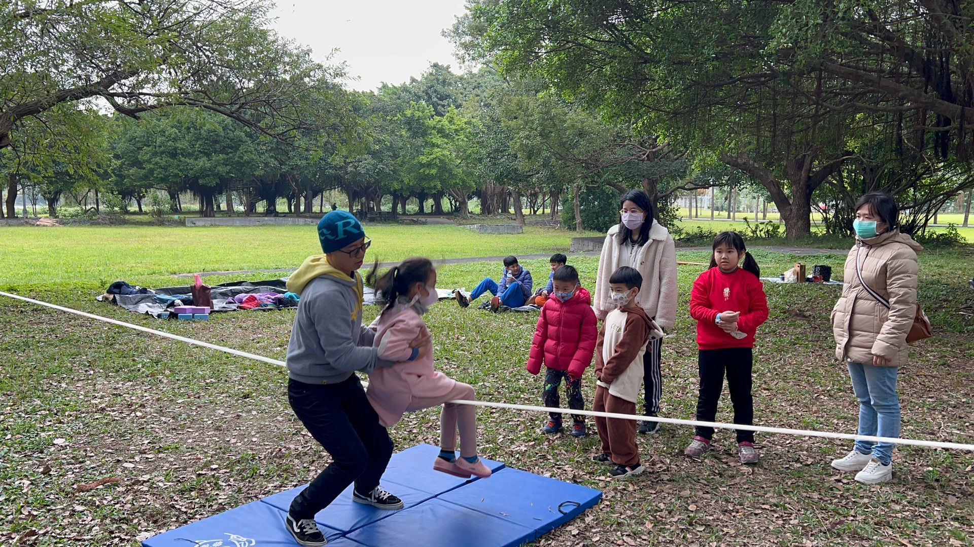 A group of children are playing on a blue mat in a park.