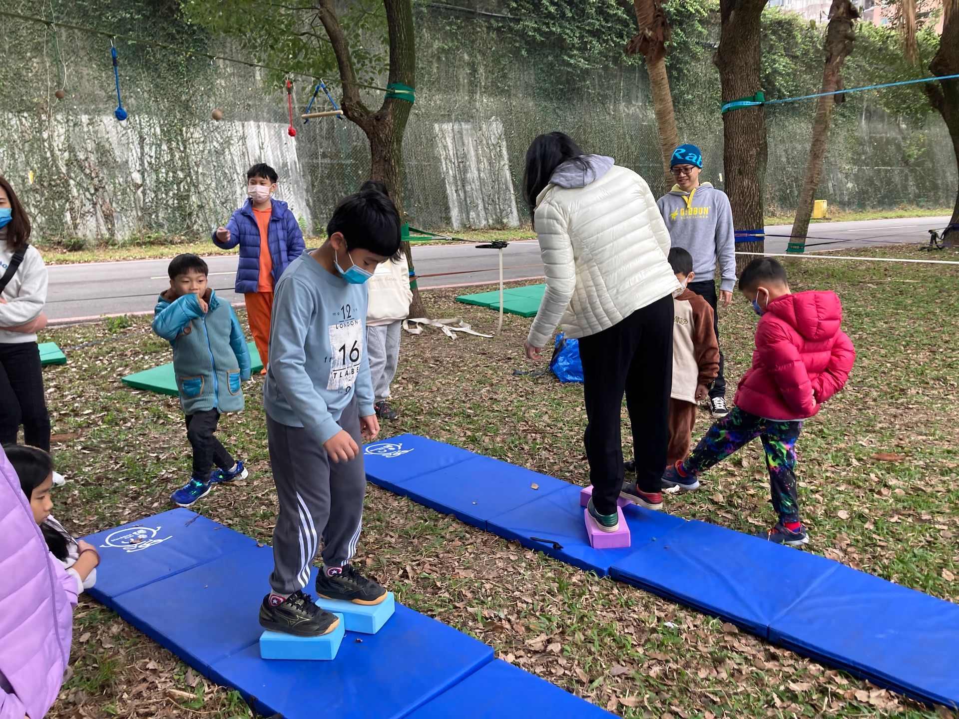 A group of children are playing on a blue mat in a park.
