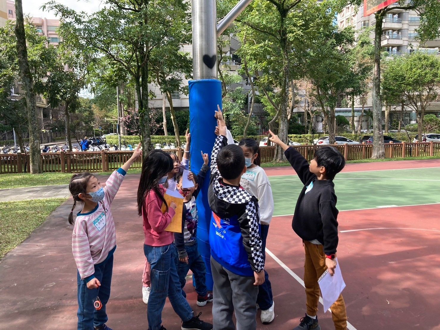 A group of children are standing around a basketball hoop in a park.