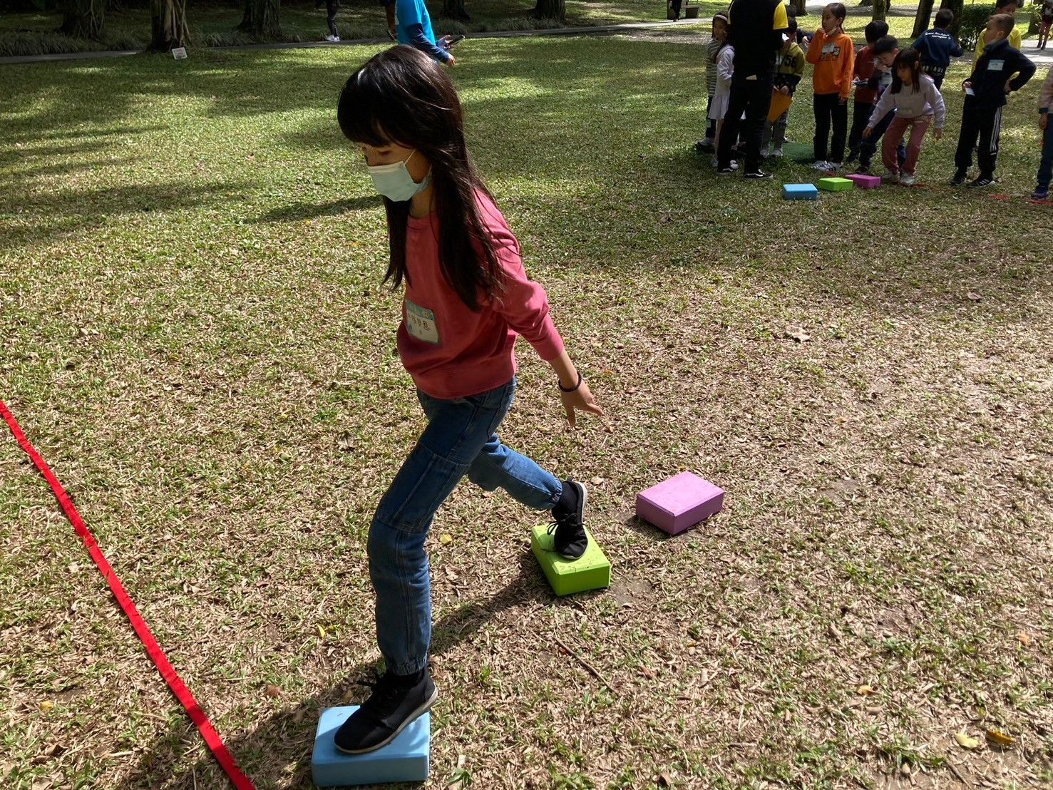 A young girl wearing a mask is standing on blocks in a park.