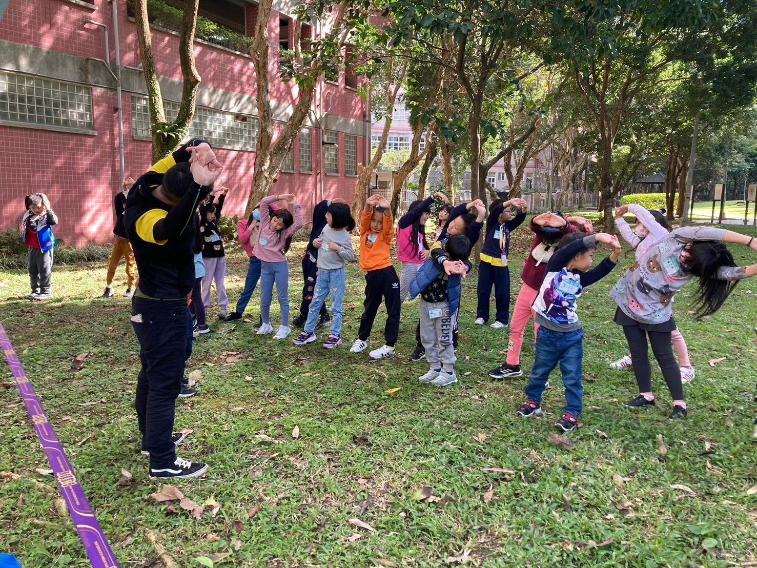 A group of children are doing stretching exercises in a park.