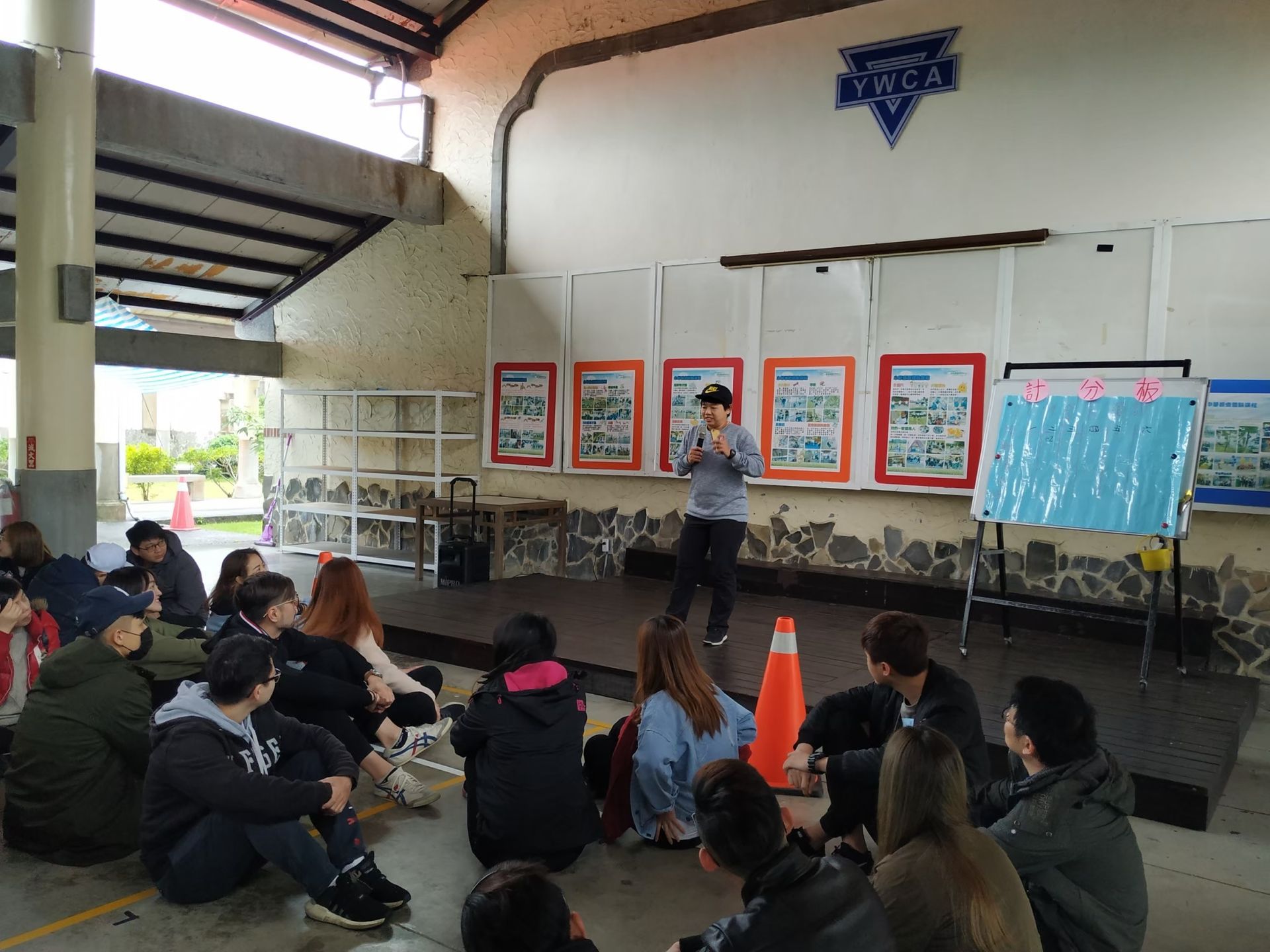 A group of people are sitting on the floor in a room while a man stands in front of them.