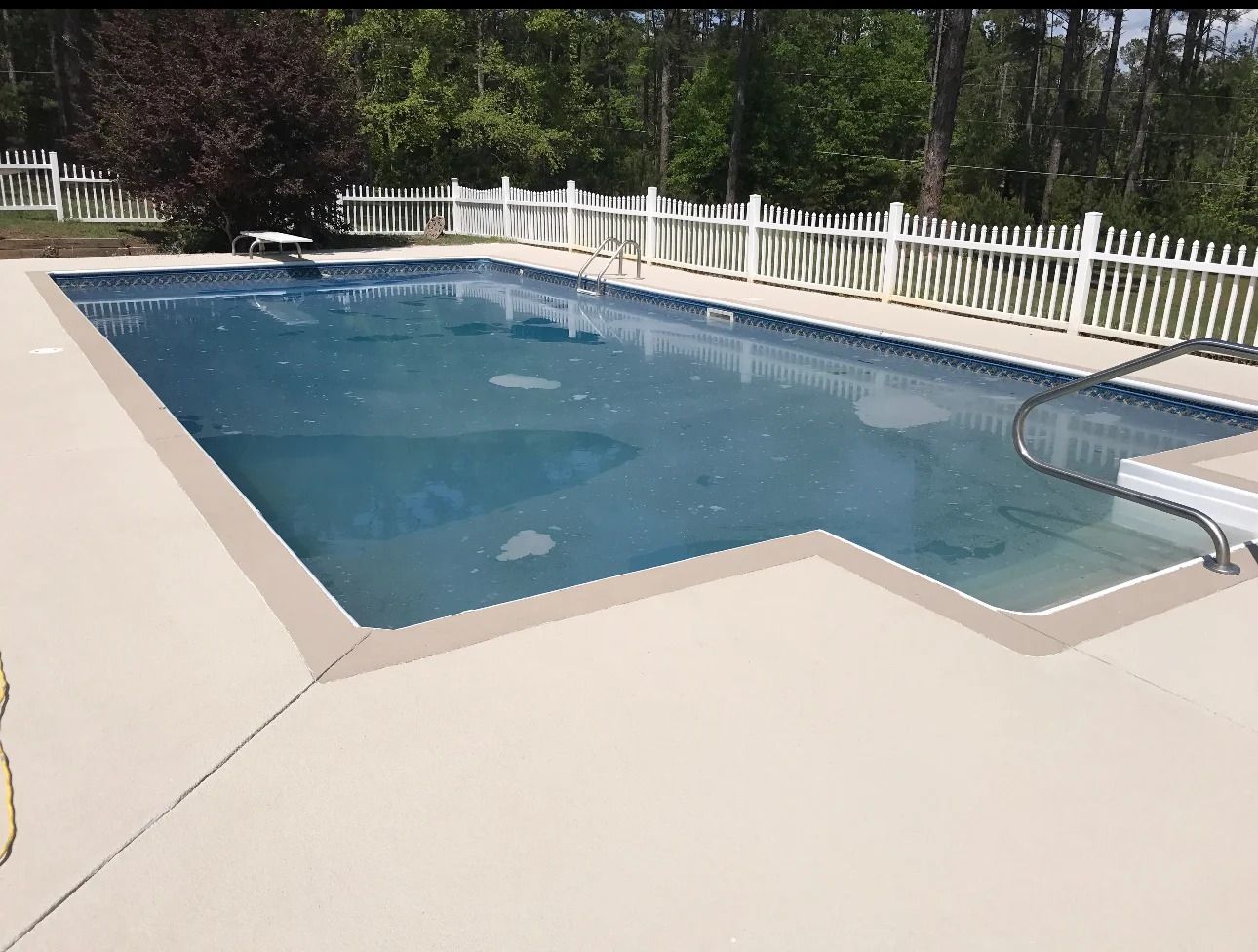 Concrete patio with textured stone pattern next to a swimming pool filled with water.