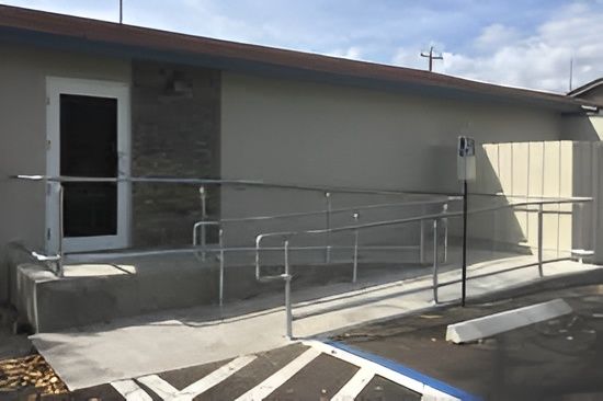 Exterior of building with wheelchair ramp, handrails, and accessible parking sign.