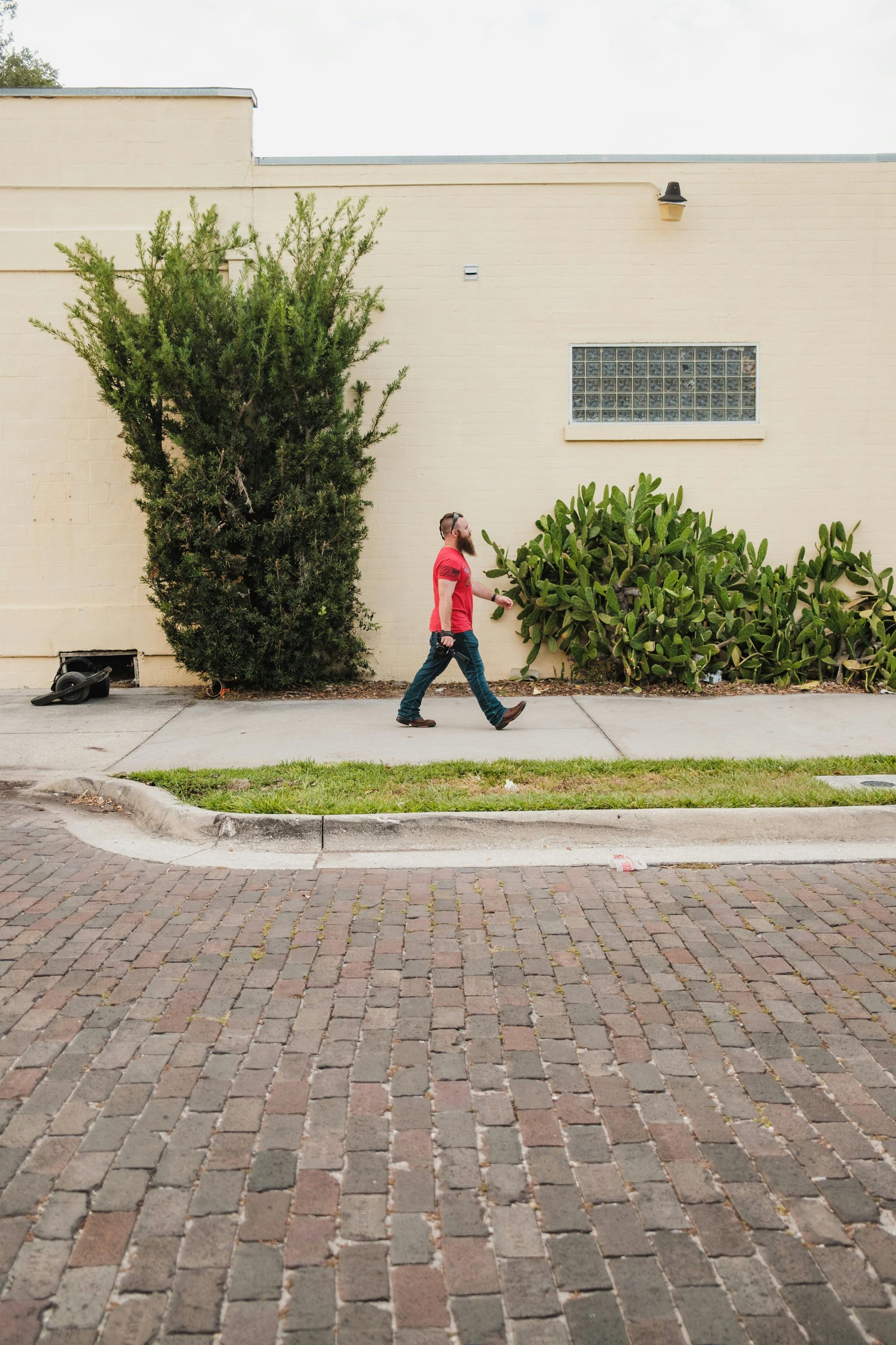 A man with a beard walks down a sidewalk next to a tan building.