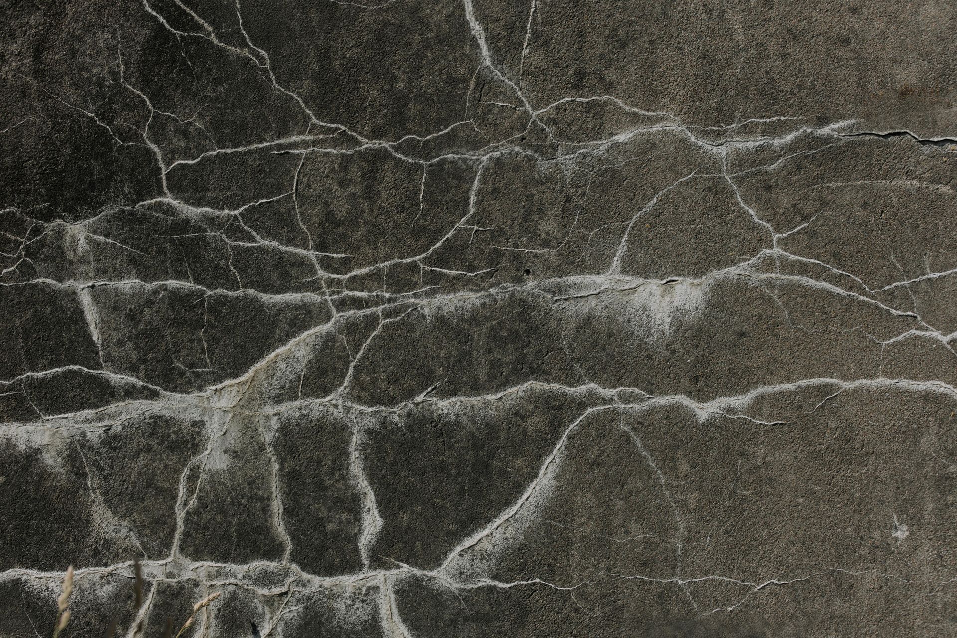 Cracked, dark gray concrete surface with white highlighting in the cracks.
