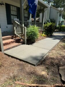 Freshly poured concrete walkway leading to a house with a porch and stairs.