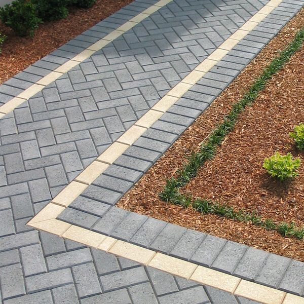 Gray brick pathway with tan border and brown mulch garden.