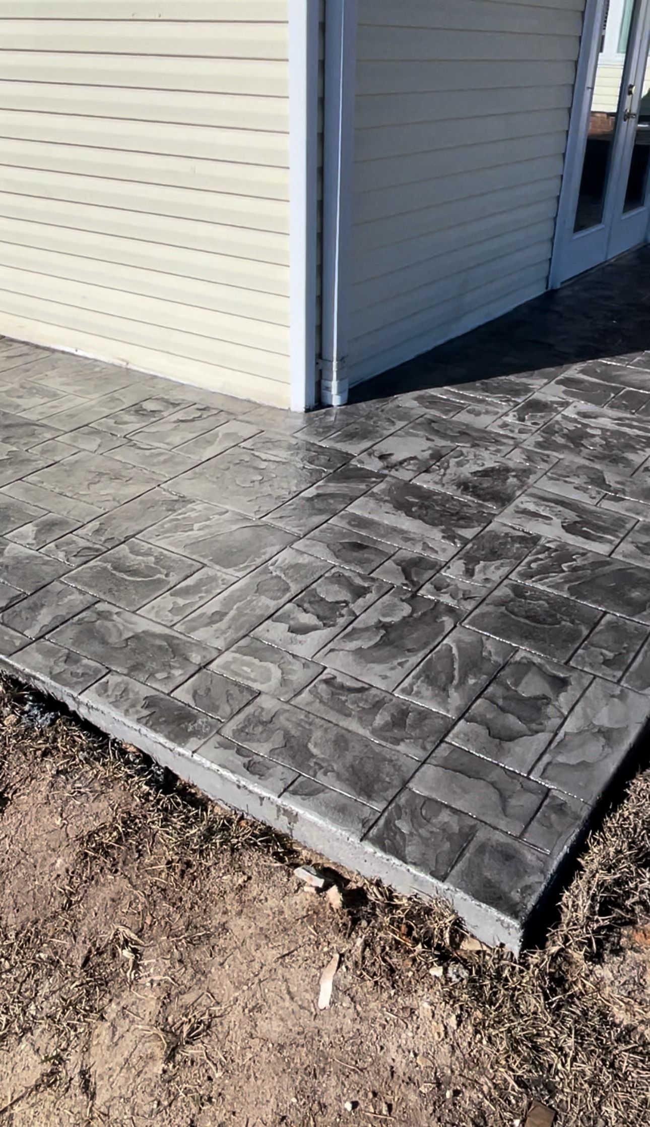 Dark gray stamped concrete patio next to a light siding building.