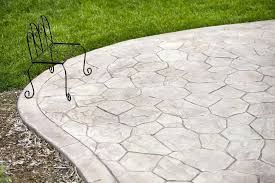 Decorative concrete patio with a rock-like pattern, bordered by grass and dirt, with a decorative metal chair.