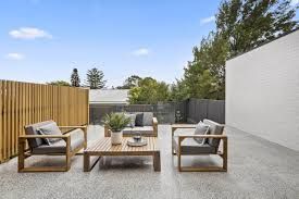 Patio with wooden furniture, grey cushions, and a concrete floor.