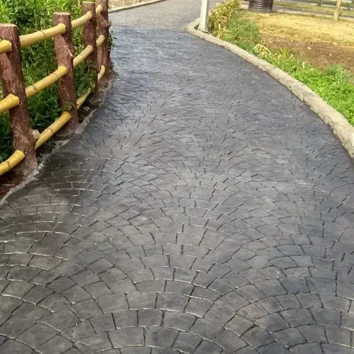 Dark gray, textured concrete walkway with a curved pattern, bordered by a wooden fence and grass.