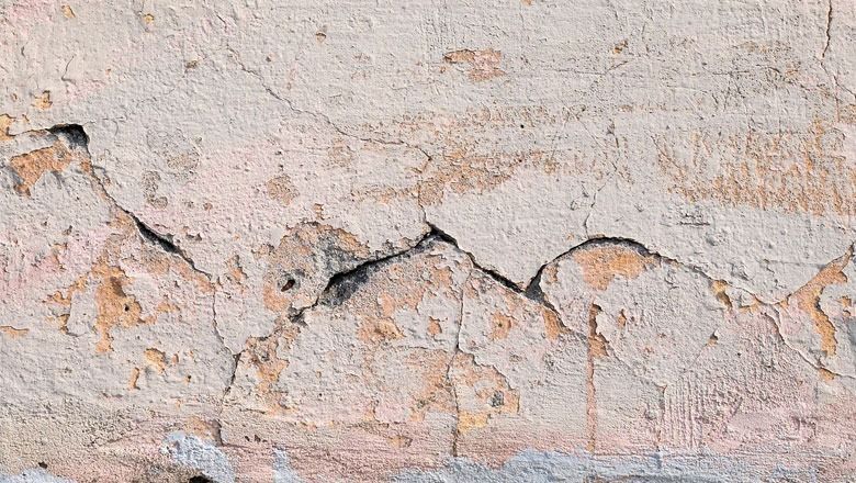 Cracked, crumbling stucco wall; beige and peach with dark crevices.