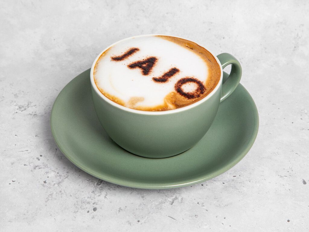 Green mug of coffee on a saucer, foam art reads 