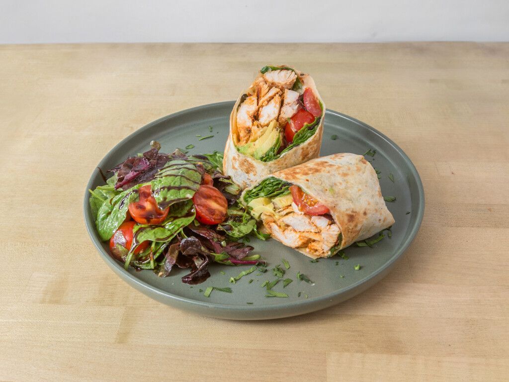 Chicken wrap and salad on a plate, with avocado and tomatoes.
