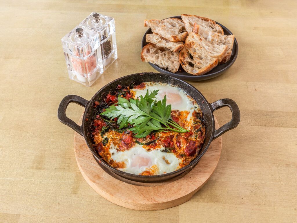 Shakshuka with bread, salt and pepper shakers on a wooden table.