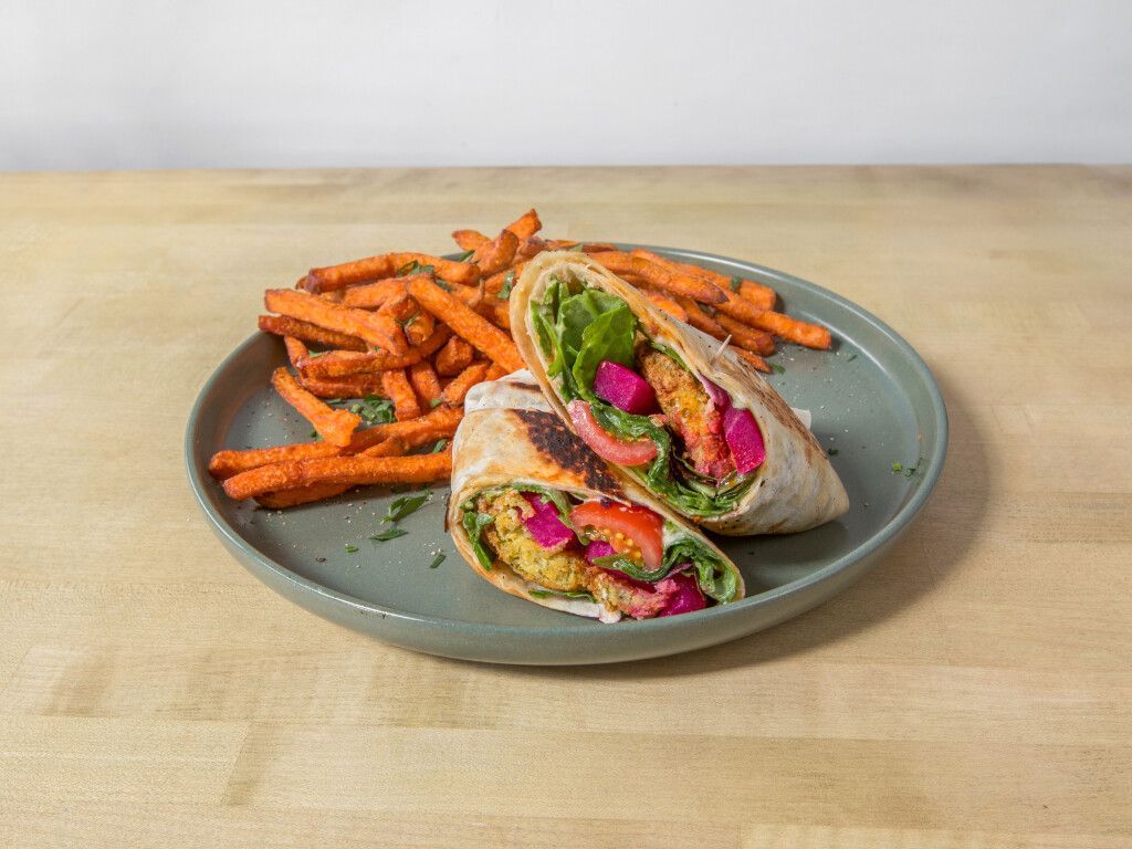 Falafel wrap and sweet potato fries on a plate, resting on a wooden surface.