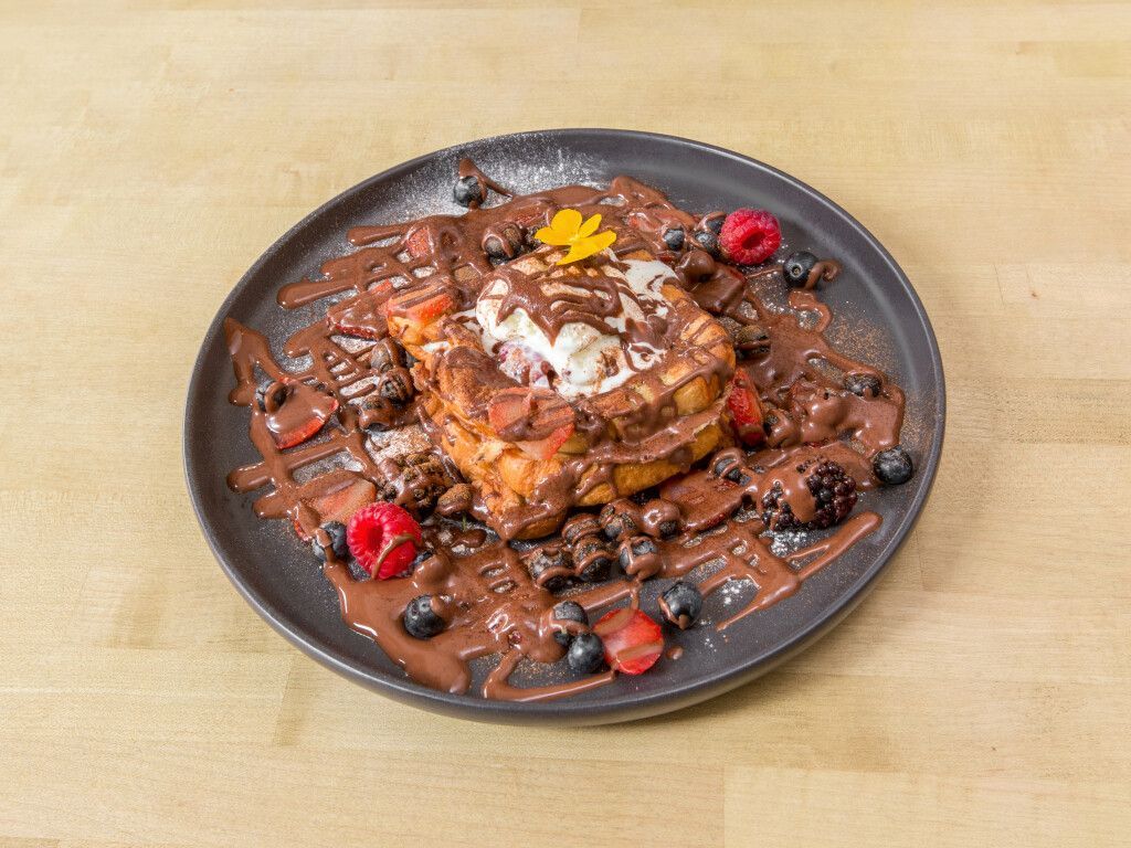 French toast with chocolate, ice cream, and berries on a black plate.